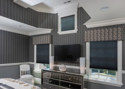 Newton homes, roman shades, cornices, gray stripe wallpaper, white coffered ceiling, gray and taupe fabrick straight valance, black honeycomb shades, Hunter Douglas Architella shades, cordless shades, cordless blinds, shades, blinds, slipcover parson chair, rectangular pillow, bedoom, mirror glass bureau, tv mounted on wall, bedroom with wallpaper, recessed lighting, white crown moldings, gray painted walls with stripe wallpaper